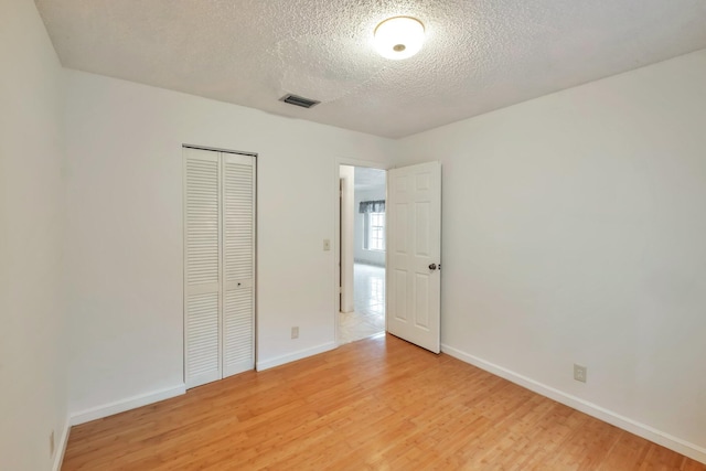 unfurnished bedroom with light wood-type flooring, a closet, and a textured ceiling