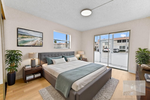 bedroom featuring multiple windows, access to exterior, a textured ceiling, and light hardwood / wood-style flooring