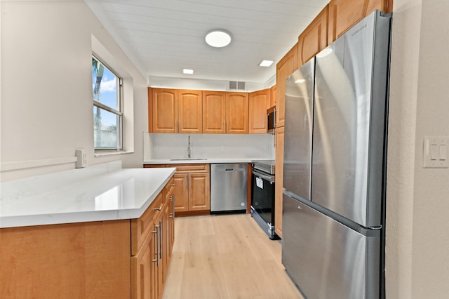 kitchen with appliances with stainless steel finishes, sink, and light wood-type flooring