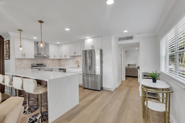 kitchen with appliances with stainless steel finishes, decorative light fixtures, sink, white cabinets, and wall chimney range hood