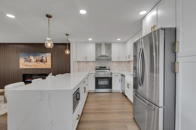 kitchen with stainless steel appliances, white cabinetry, pendant lighting, and wall chimney range hood