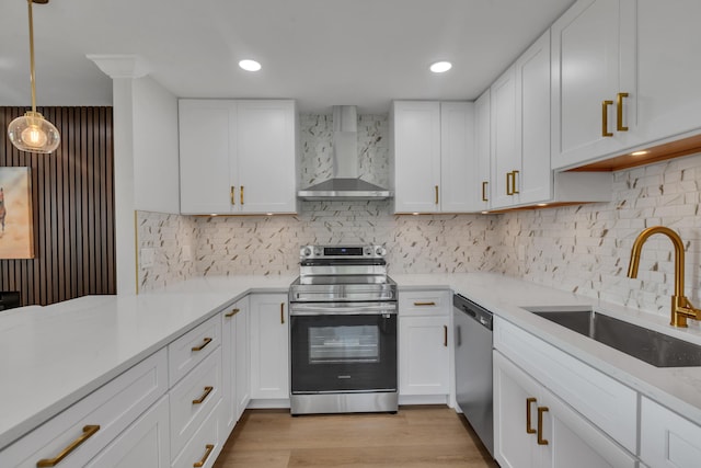 kitchen featuring white cabinetry, sink, hanging light fixtures, stainless steel appliances, and wall chimney range hood