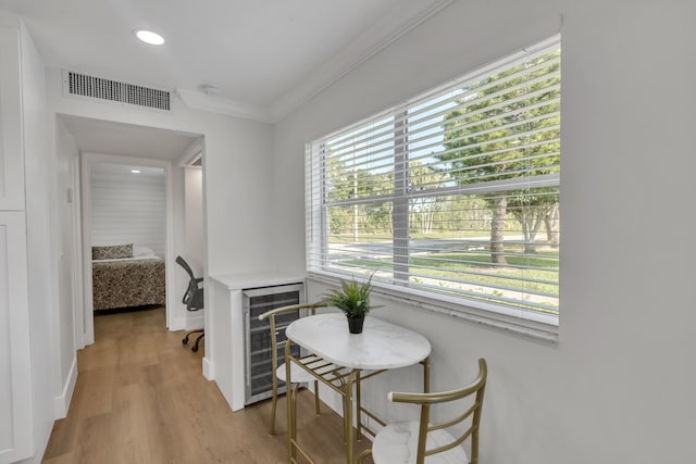 corridor with ornamental molding, a healthy amount of sunlight, beverage cooler, and light hardwood / wood-style floors