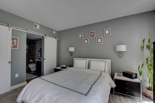 bedroom with connected bathroom, a barn door, and hardwood / wood-style flooring