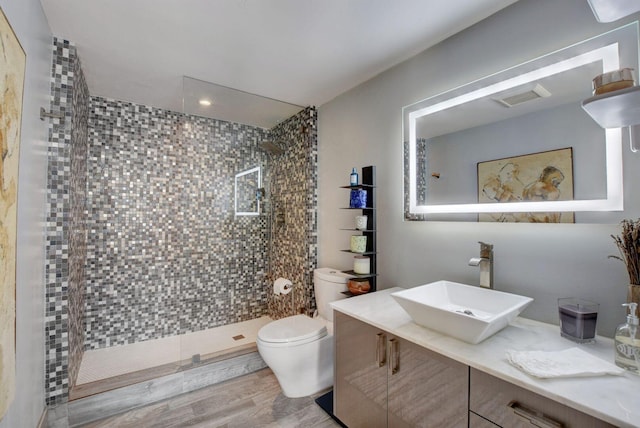 bathroom featuring toilet, vanity, hardwood / wood-style floors, and a tile shower