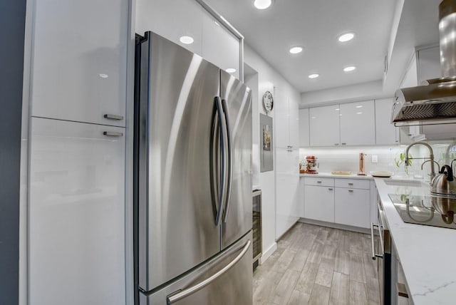 kitchen featuring backsplash, light wood-type flooring, light stone countertops, white cabinets, and stainless steel refrigerator