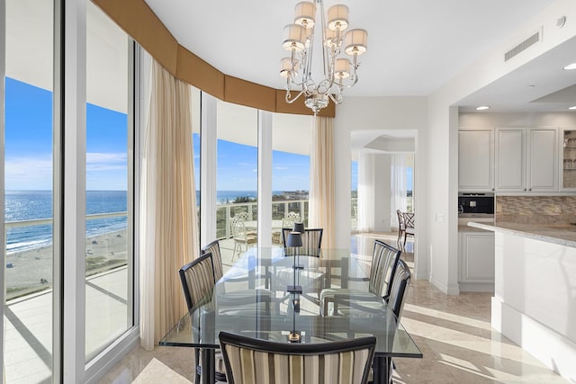 dining space with a view of the beach, a notable chandelier, and a water view