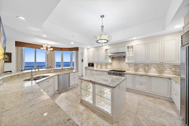 kitchen with pendant lighting, sink, appliances with stainless steel finishes, a water view, and a tray ceiling