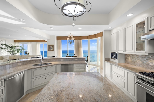 kitchen featuring sink, a tray ceiling, stainless steel appliances, a water view, and an inviting chandelier