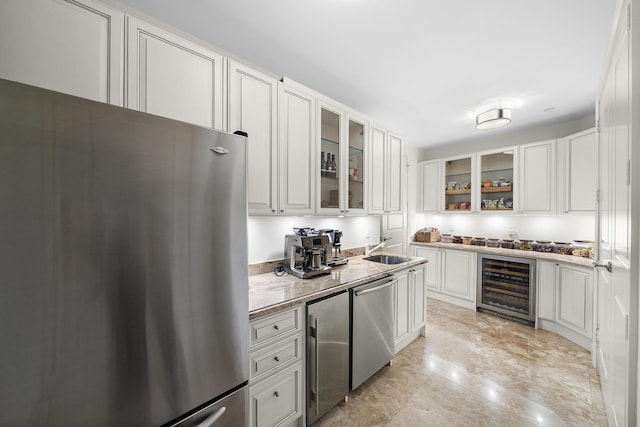 kitchen with sink, appliances with stainless steel finishes, white cabinetry, wine cooler, and light stone counters