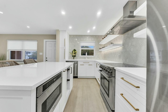 kitchen featuring light hardwood / wood-style floors, extractor fan, appliances with stainless steel finishes, tasteful backsplash, and white cabinets