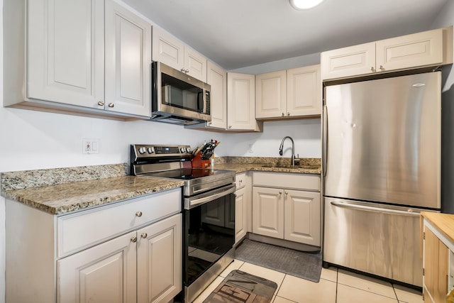 kitchen with light tile patterned floors, sink, light stone counters, and stainless steel appliances