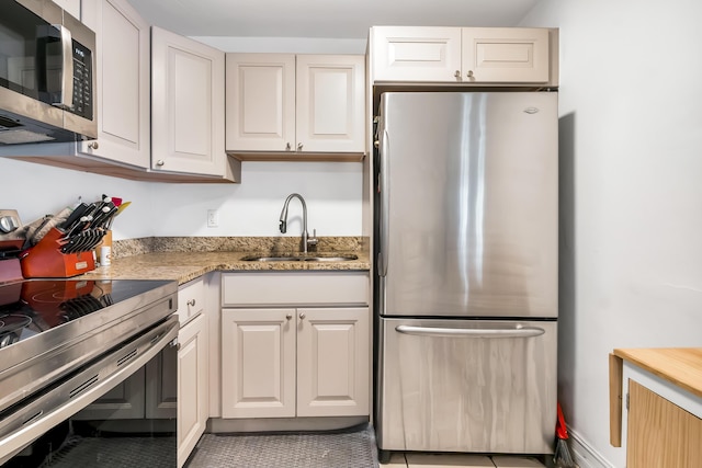 kitchen featuring white cabinets, appliances with stainless steel finishes, sink, light stone counters, and light tile patterned floors