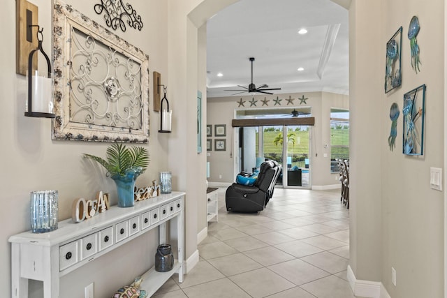 corridor featuring ornamental molding, a tray ceiling, and light tile patterned floors