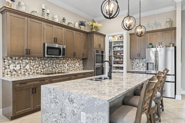 kitchen with sink, appliances with stainless steel finishes, backsplash, light stone countertops, and an island with sink