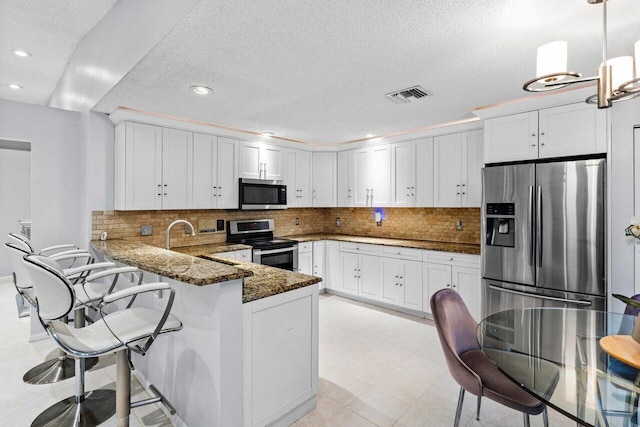 kitchen featuring kitchen peninsula, decorative light fixtures, backsplash, dark stone counters, and stainless steel appliances