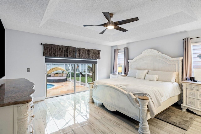 bedroom featuring light wood-type flooring, ceiling fan, a raised ceiling, and access to outside