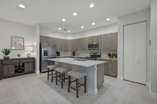 kitchen featuring appliances with stainless steel finishes, a kitchen bar, sink, light tile patterned flooring, and a center island with sink