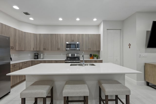 kitchen featuring sink, stainless steel appliances, a kitchen island with sink, and a breakfast bar