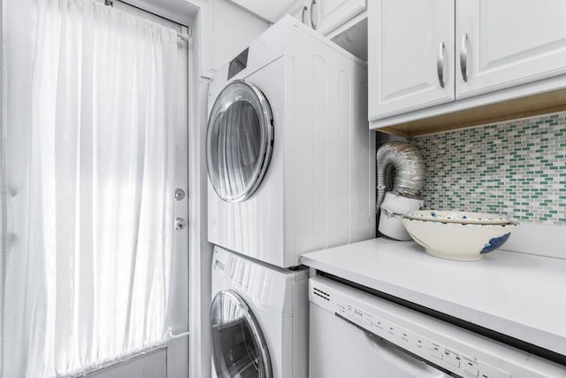 clothes washing area featuring stacked washing maching and dryer and cabinets