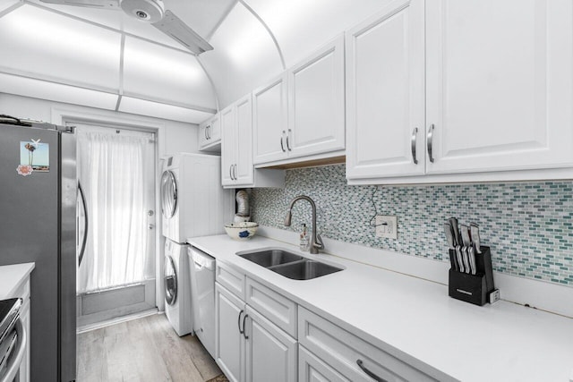 kitchen featuring white cabinets, decorative backsplash, sink, stainless steel fridge, and stacked washing maching and dryer