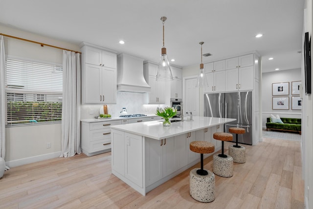 kitchen featuring premium range hood, white cabinetry, hanging light fixtures, a center island with sink, and stainless steel appliances