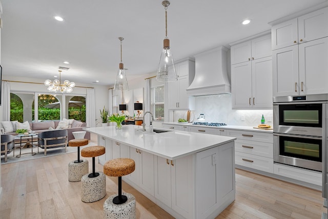 kitchen with appliances with stainless steel finishes, an island with sink, white cabinets, decorative backsplash, and custom range hood