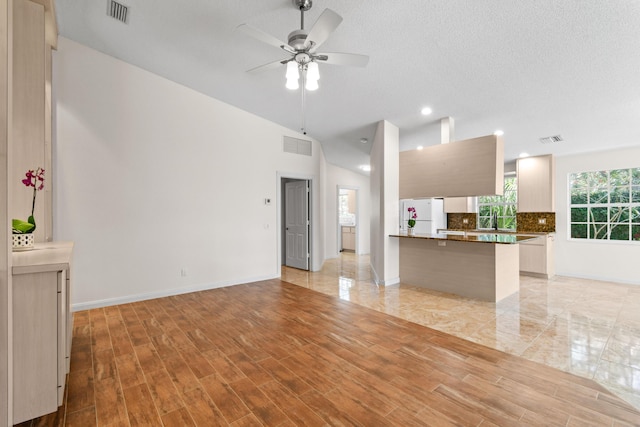 unfurnished living room featuring vaulted ceiling, ceiling fan, a textured ceiling, and sink