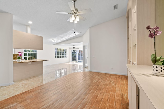 unfurnished living room featuring ceiling fan, a textured ceiling, and vaulted ceiling