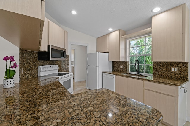 kitchen featuring kitchen peninsula, sink, white appliances, light brown cabinetry, and dark stone counters