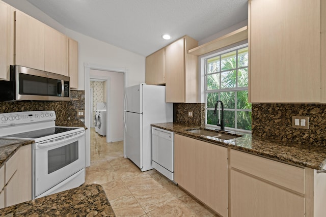 kitchen with light brown cabinetry, dark stone counters, sink, and white appliances