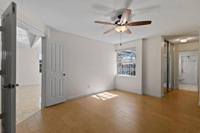 unfurnished room with ceiling fan, light wood-type flooring, and a textured ceiling