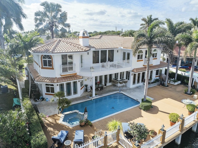 back of house with a swimming pool with hot tub, cooling unit, a balcony, and a patio