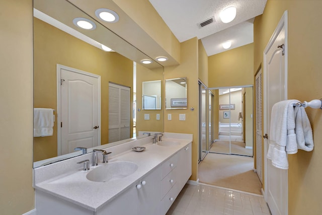 bathroom with tile patterned floors, vanity, a textured ceiling, and lofted ceiling