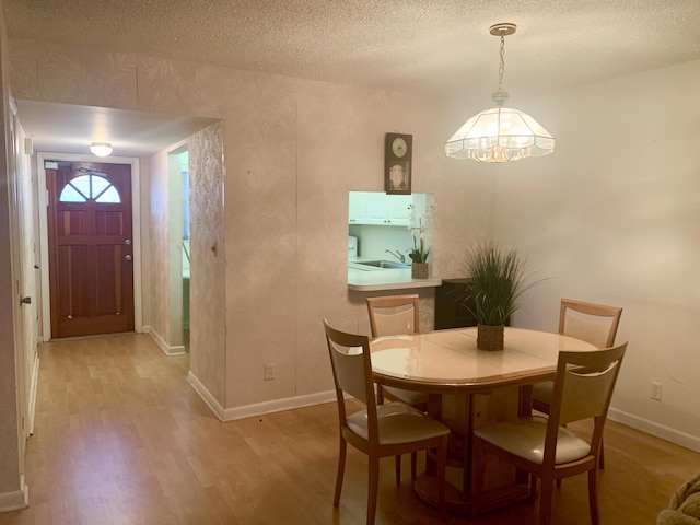 dining area with a textured ceiling, sink, light hardwood / wood-style floors, and a notable chandelier