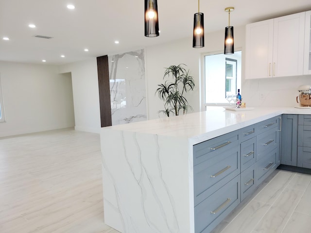 kitchen featuring backsplash, white cabinets, hanging light fixtures, and light stone countertops