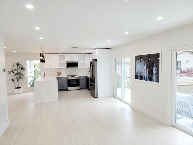 kitchen featuring white cabinetry, appliances with stainless steel finishes, decorative light fixtures, light wood-type flooring, and light stone counters