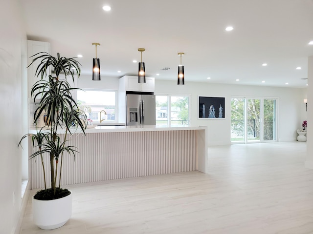 kitchen with decorative light fixtures, sink, white cabinetry, light wood-type flooring, and stainless steel fridge