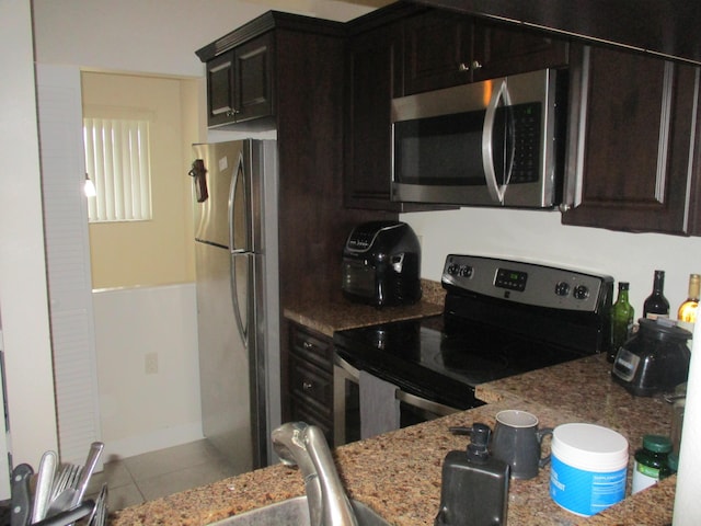 kitchen featuring dark brown cabinets, stainless steel appliances, light stone countertops, and light tile patterned flooring