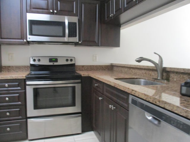 kitchen with dark brown cabinetry, appliances with stainless steel finishes, a sink, and light tile patterned flooring