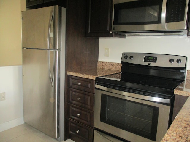 kitchen featuring appliances with stainless steel finishes, dark brown cabinets, light stone counters, and light tile patterned floors