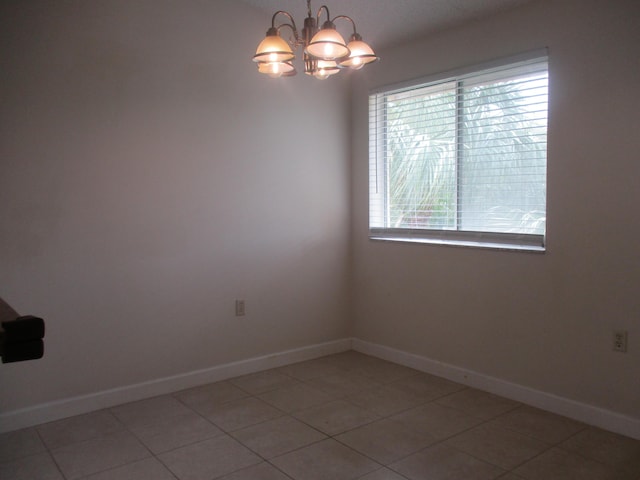 spare room featuring a chandelier, light tile patterned floors, and baseboards