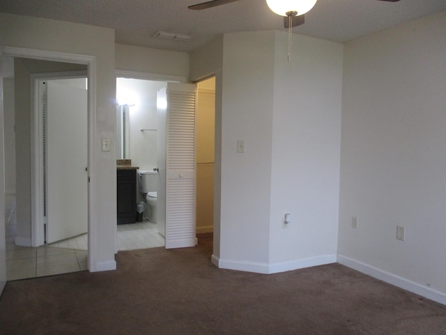 unfurnished bedroom with baseboards, ceiling fan, ensuite bathroom, carpet, and tile patterned flooring