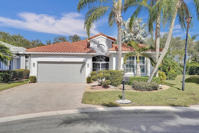 mediterranean / spanish house featuring a front yard, an attached garage, stucco siding, a tile roof, and decorative driveway