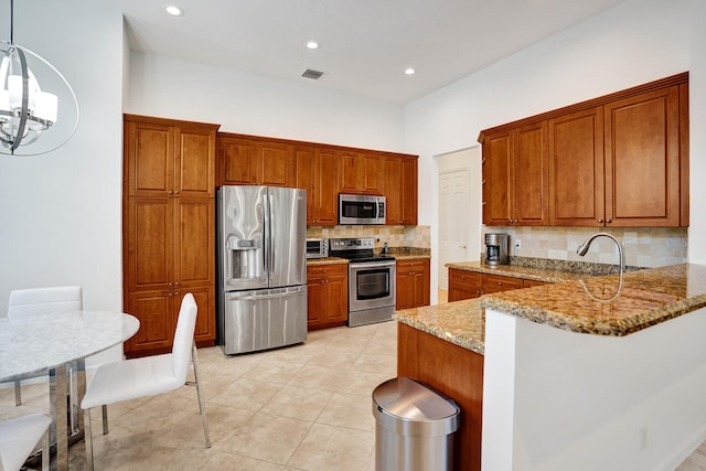 kitchen with pendant lighting, appliances with stainless steel finishes, tasteful backsplash, kitchen peninsula, and light stone counters