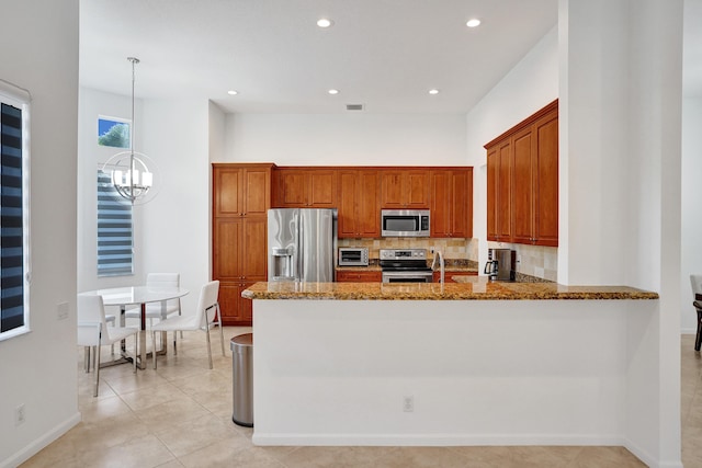 kitchen with light stone countertops, decorative light fixtures, stainless steel appliances, kitchen peninsula, and light tile patterned floors