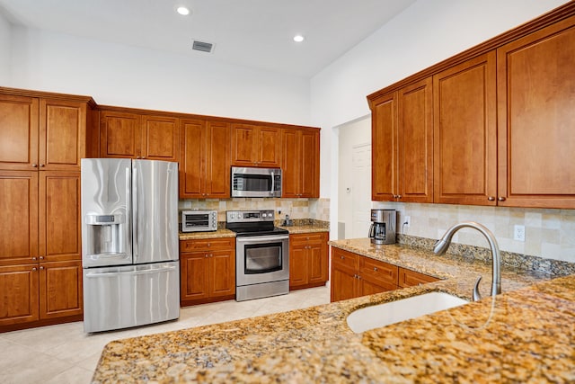 kitchen featuring tasteful backsplash, sink, appliances with stainless steel finishes, light tile patterned floors, and light stone counters