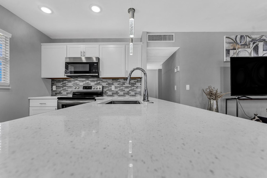 kitchen featuring pendant lighting, sink, white cabinetry, appliances with stainless steel finishes, and light stone counters