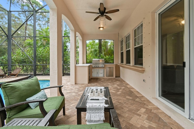 view of patio / terrace featuring ceiling fan, a swimming pool, glass enclosure, a grill, and exterior kitchen