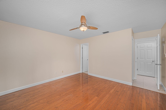 empty room featuring ceiling fan, light wood-type flooring, and a textured ceiling